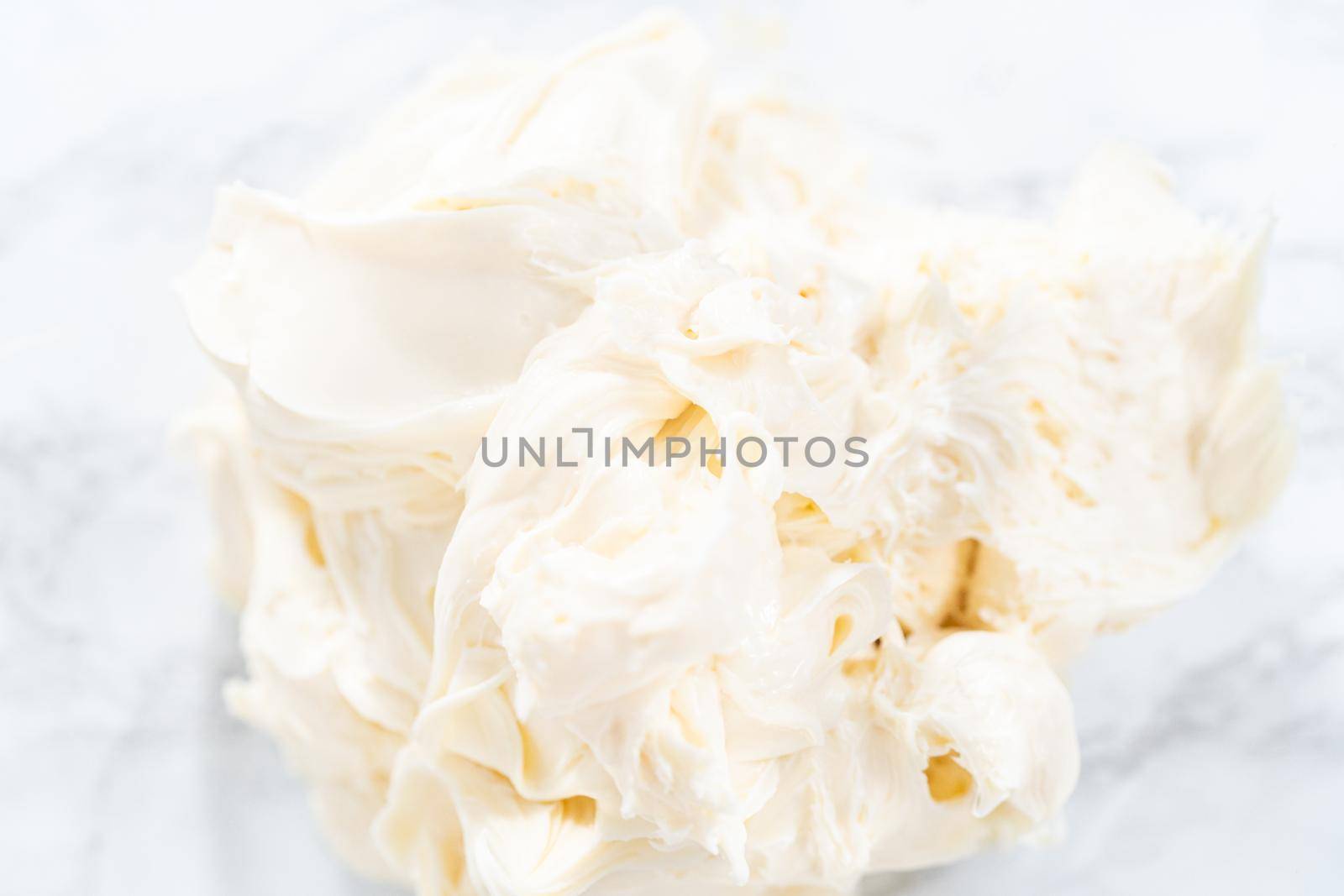 Mixing store-bought vanilla frosting in a mixing glass bowl with a hand mixer.