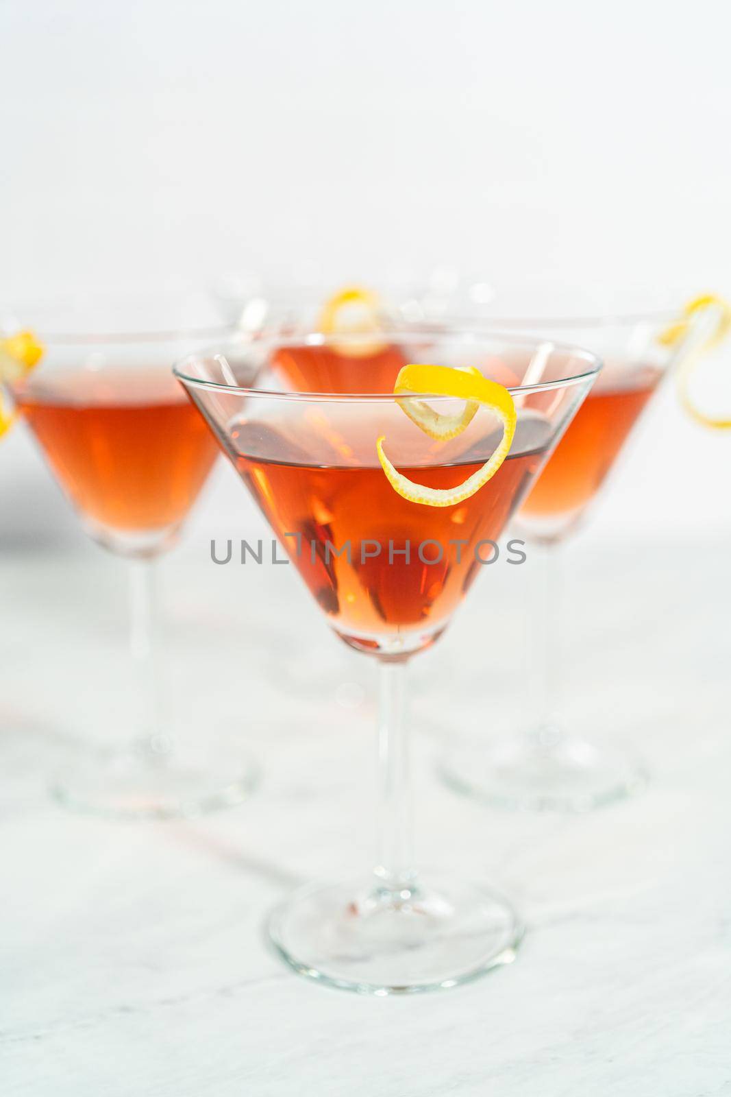 Cosmopolitan cocktail in a martini glass and decorated with a lemon swirl.