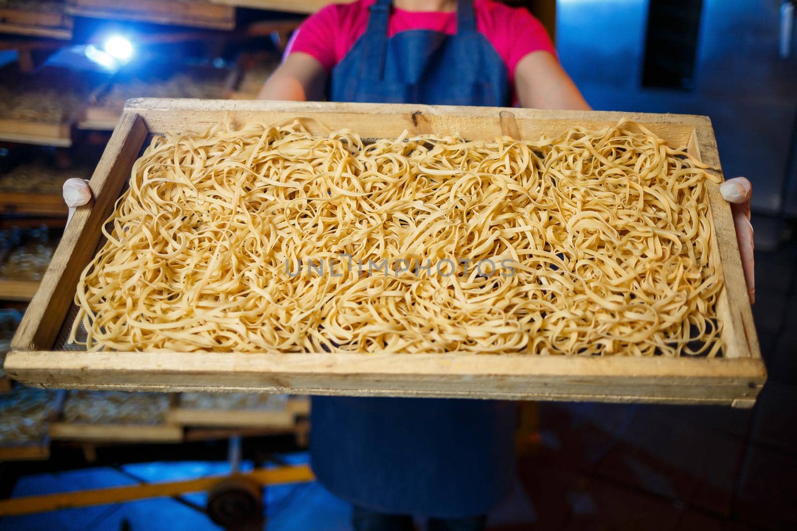 The girl works on the production of spaghetti. Making noodles. Pasta factory. Stage production of pasta. Raw noodles. Worker with a box of pasta.