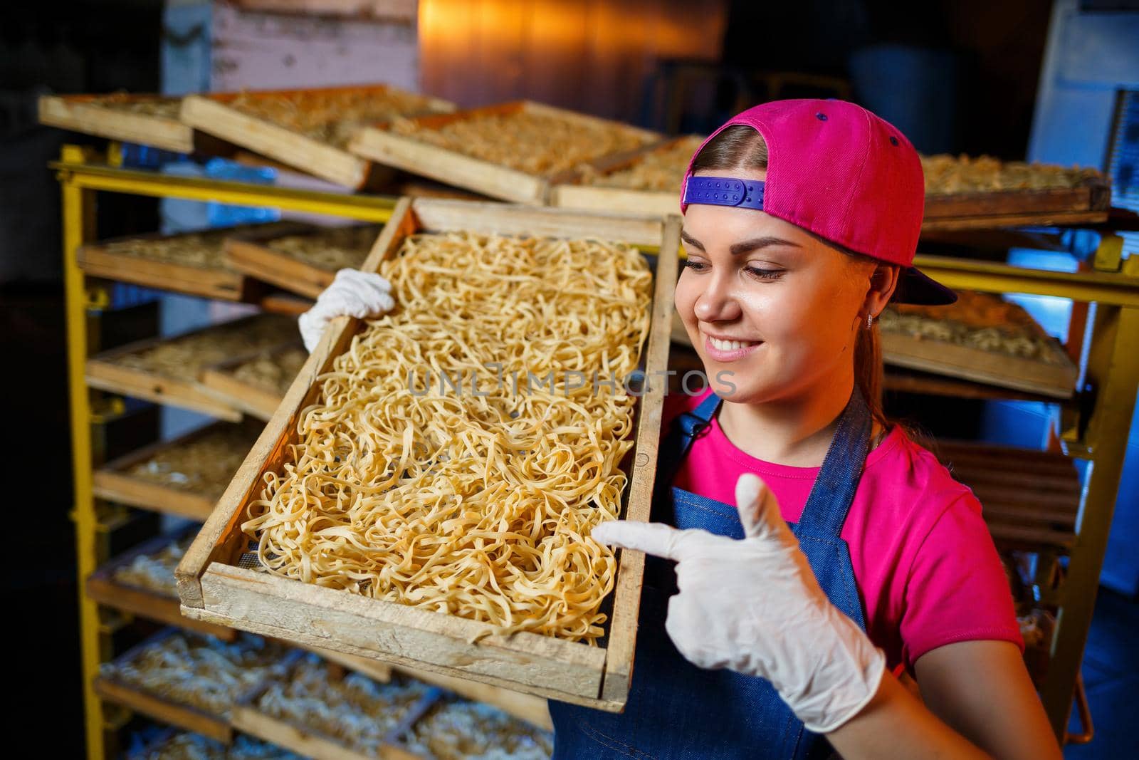 The girl works on the production of spaghetti. Making noodles. Pasta factory. Stage production of pasta. Raw noodles. Worker with a box of pasta.