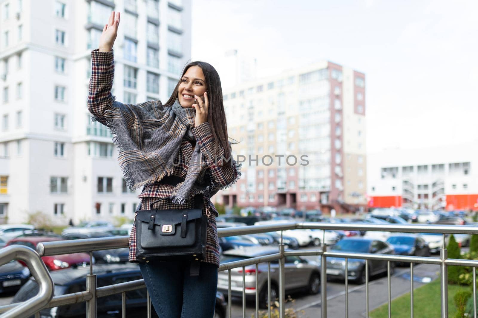 young woman talking on the phone waving her hand to her friend with a smile on her face.