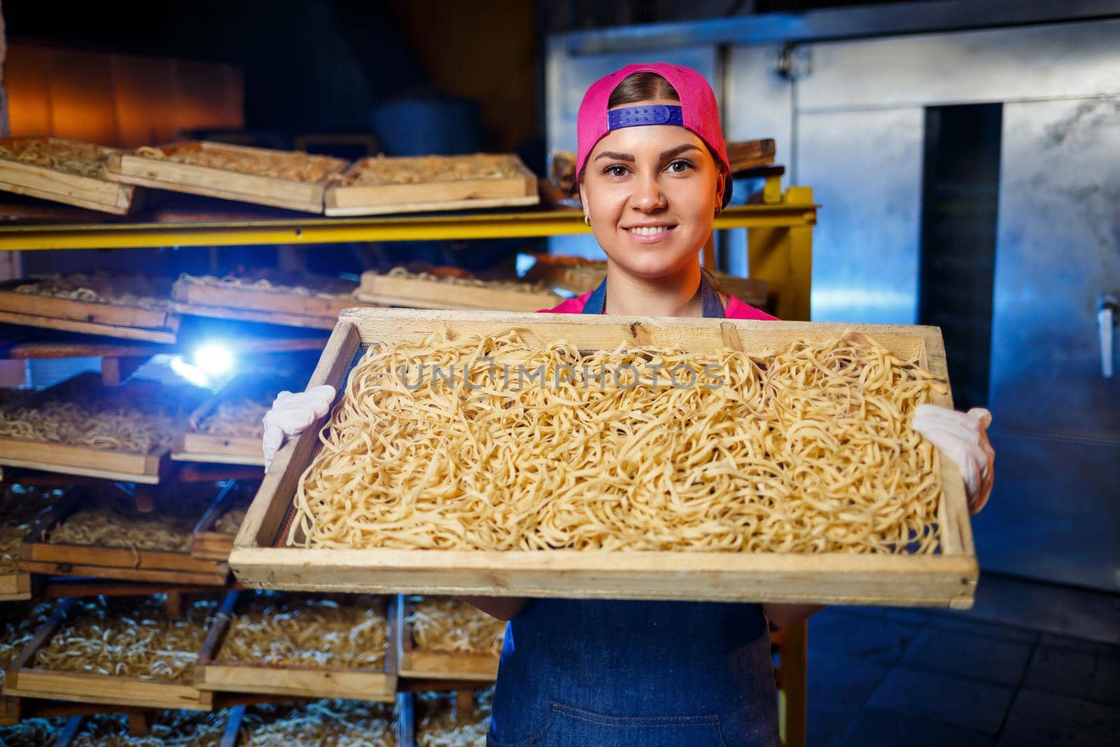 The girl works on the production of spaghetti. Making noodles. Pasta factory. Stage production of pasta. Raw noodles. Worker with a box of pasta.