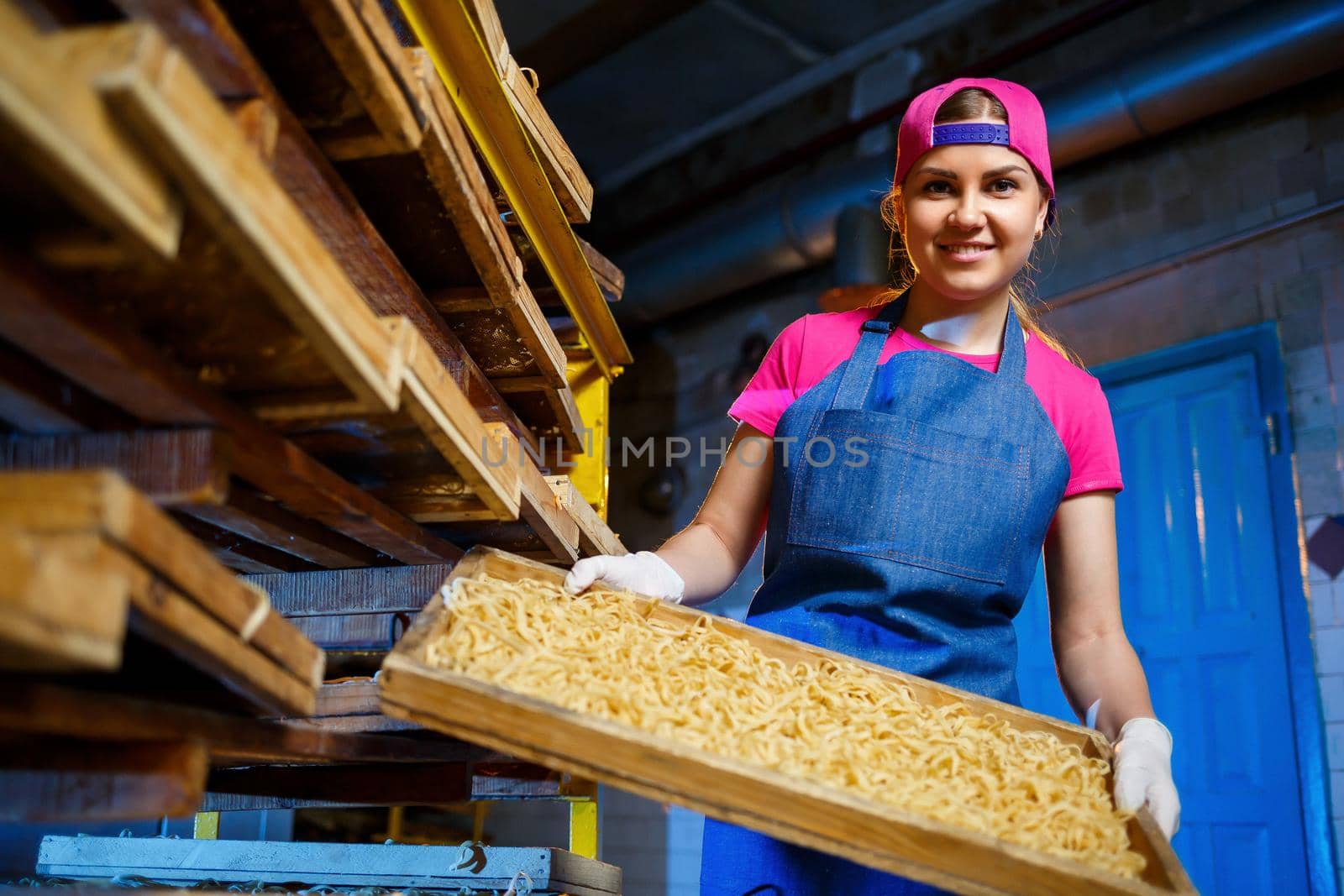 The girl works on the production of spaghetti. Making noodles. Pasta factory. Stage production of pasta. Raw noodles. Worker with a box of pasta.