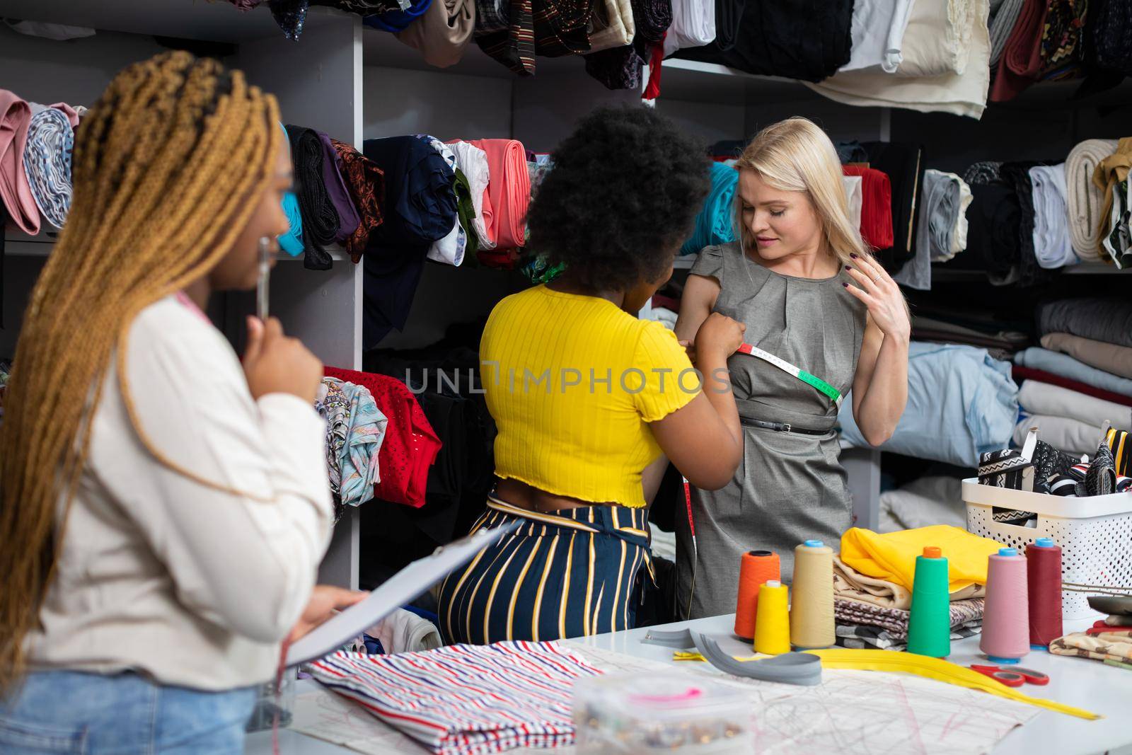 Measurement of chest circumference taken by a dark-skinned seamstress. Two African women and a European woman in a tailor's workshop.