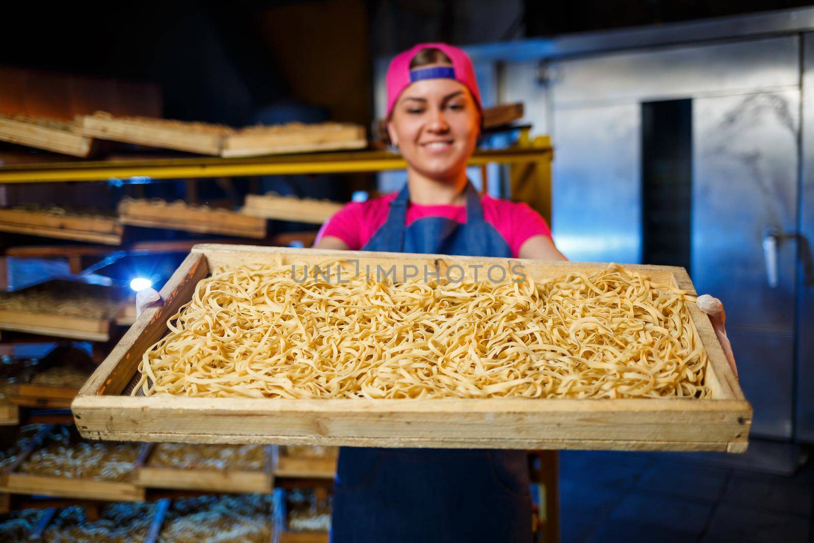 The girl works on the production of spaghetti. Making noodles. Pasta factory. Stage production of pasta. Raw noodles. Worker with a box of pasta.
