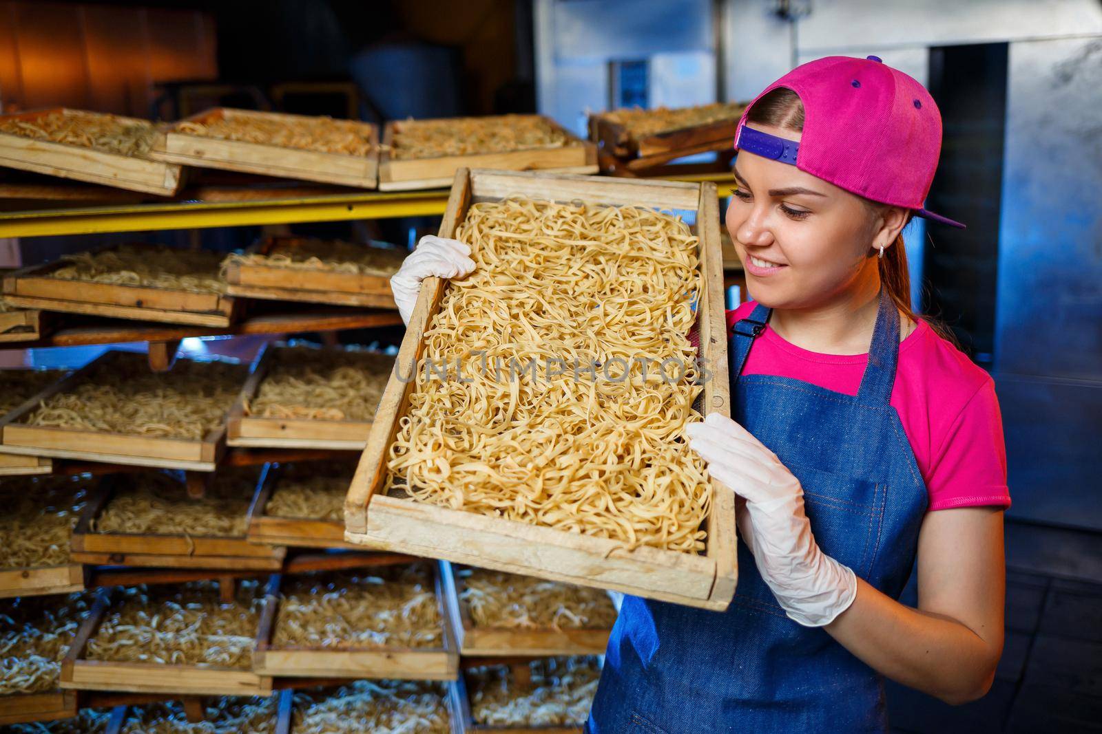 The girl works on the production of spaghetti. Making noodles. Pasta factory. Stage production of pasta. Raw noodles. Worker with a box of pasta.