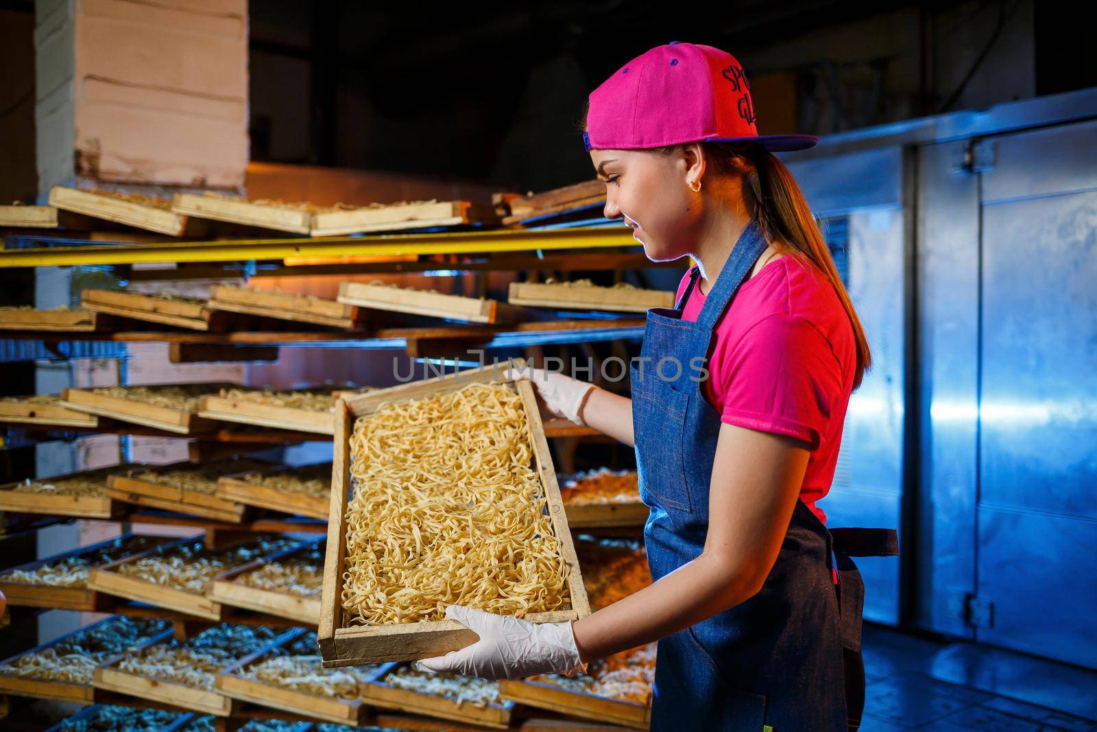The girl works on the production of spaghetti. Making noodles. Pasta factory. Stage production of pasta. Raw noodles. Worker with a box of pasta.