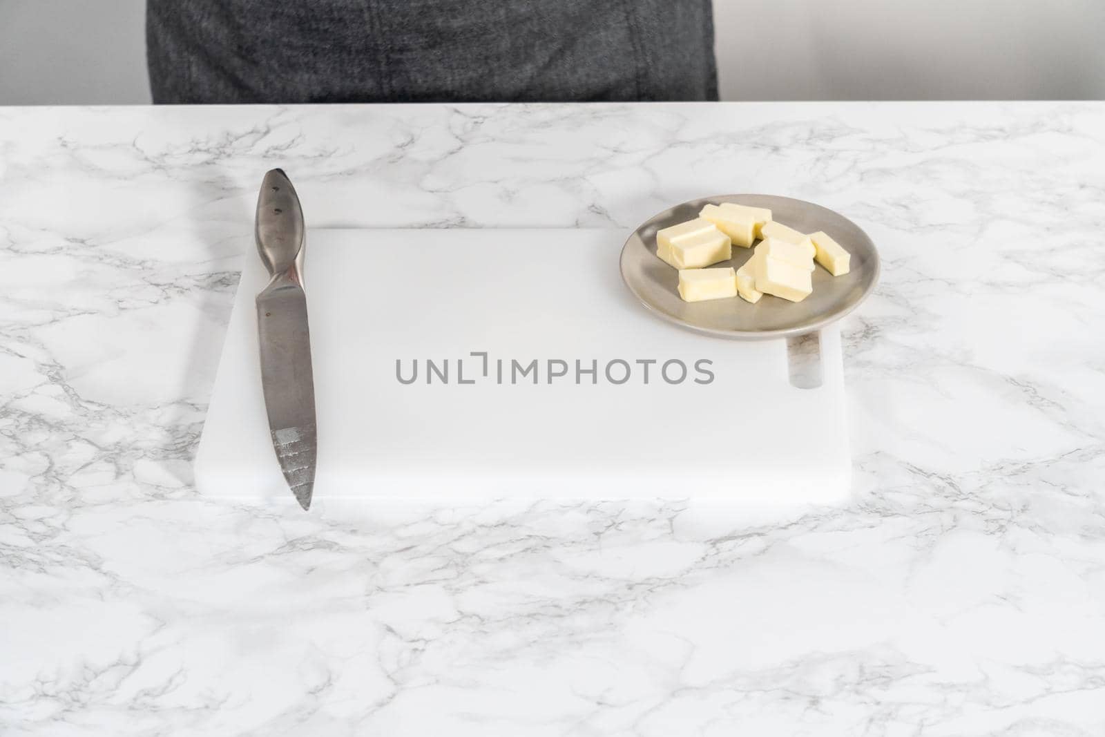 Slicing sticks of unsalted butter on a white cutting board.