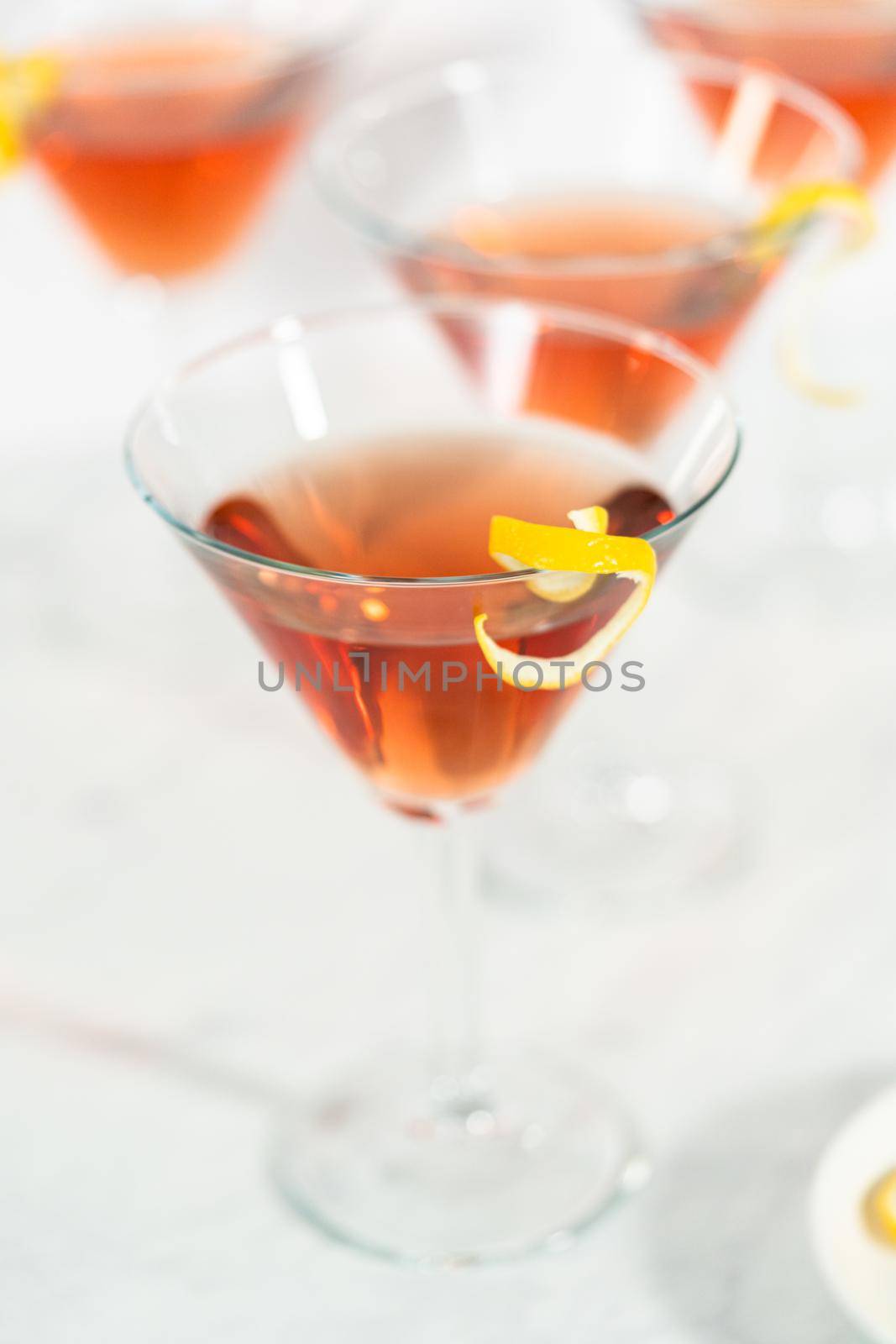 Cosmopolitan cocktail in a martini glass and decorated with a lemon swirl.