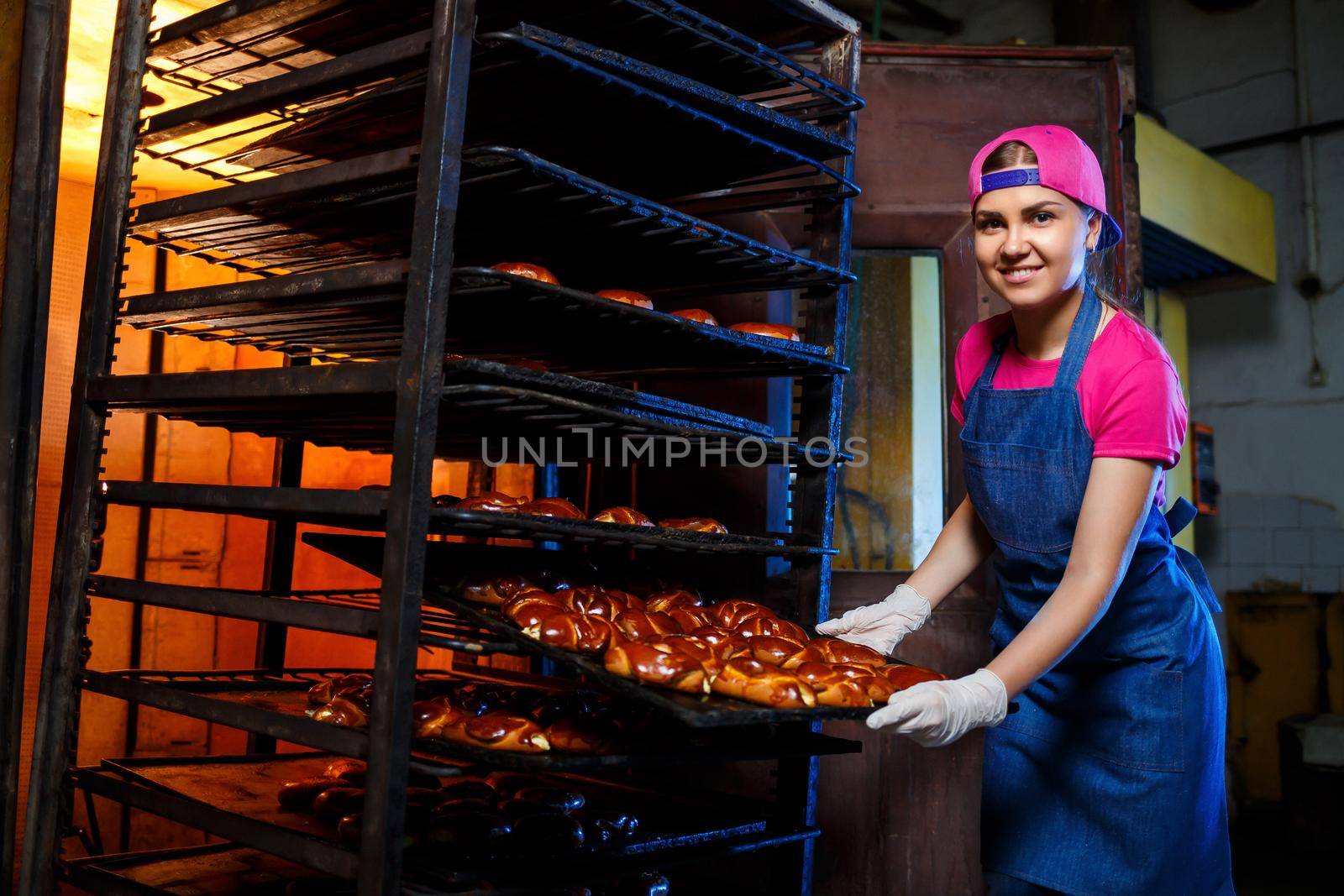 Girl baker holds a tray with hot pastries in the bakery. Production of bakery products. Fresh crispy pastry rack