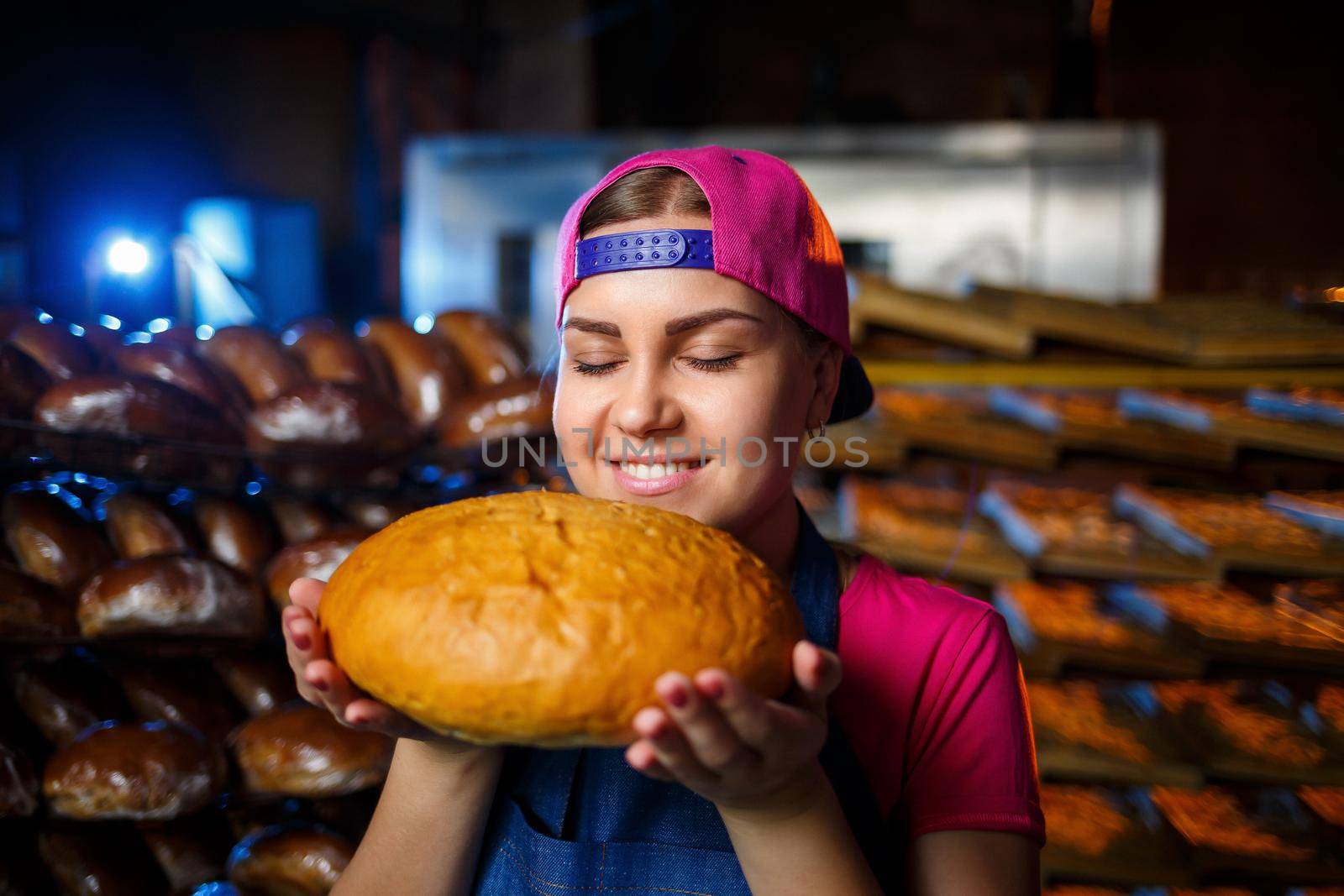 The stage of baking in a bakery. Portrait of a baker girl with bread in her hands against the background of shelving in a bakery. Hands of a baker with bread. Industrial bread production