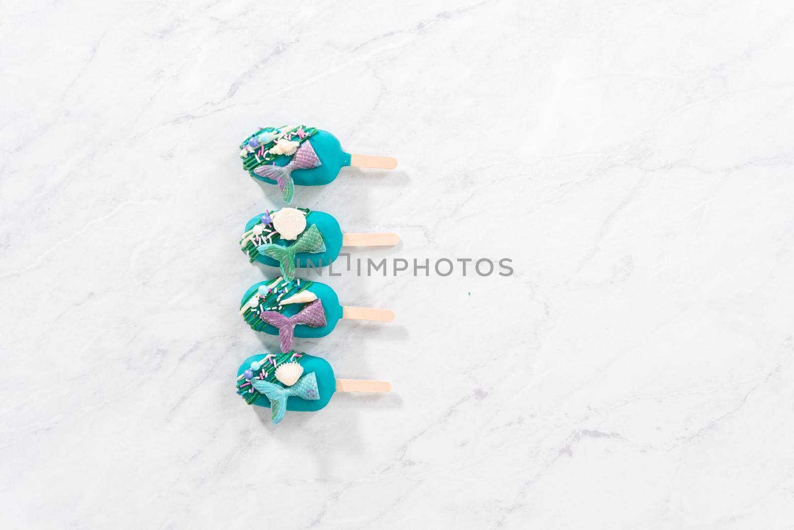 Flat lay. Mermaid cakesicles with drizzled chocolate, chocolate mermaid tails, seashells, and sprinkles.