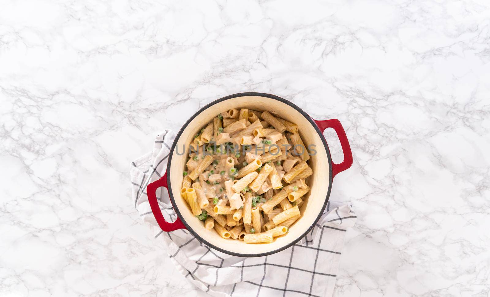 Flat lay. Mixing ingredients in an enameled dutch oven to prepare chicken alfredo pasta.