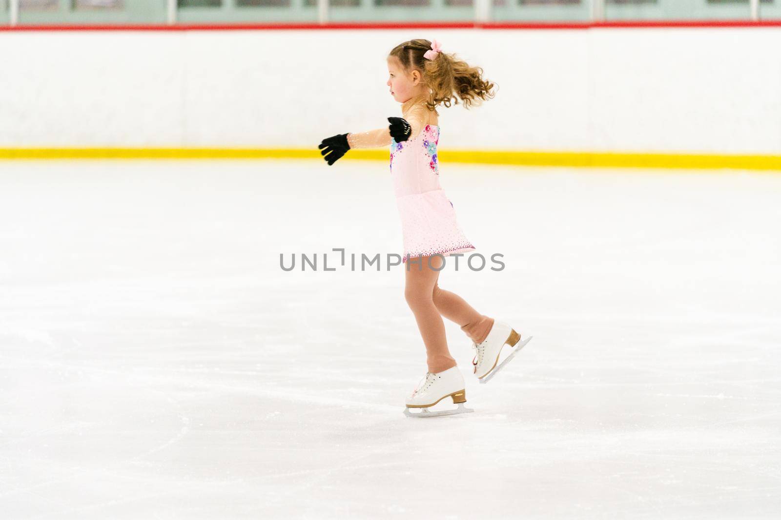 Little girl practicing figure skating on an indoor ice skating rink.