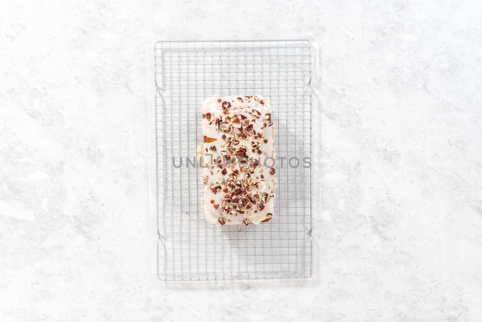 Flat lay. Glazing pumpkin bread with a white glaze and garnishing with shopped pecans.