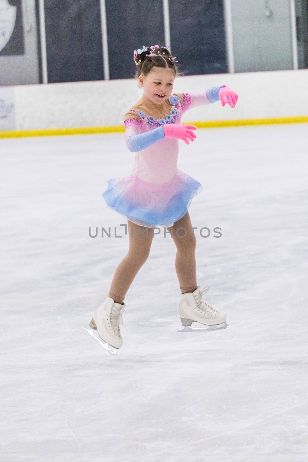 Little girl practicing figure skating on an indoor ice rink.