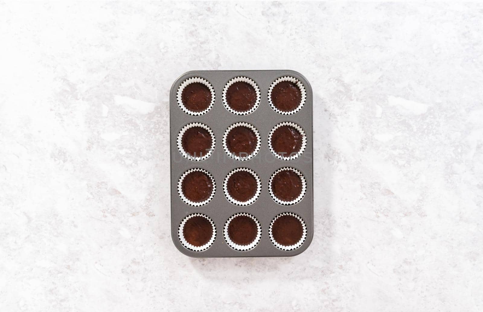 Flat lay. Scooping chocolate cupcake dough into the cupcake liners.