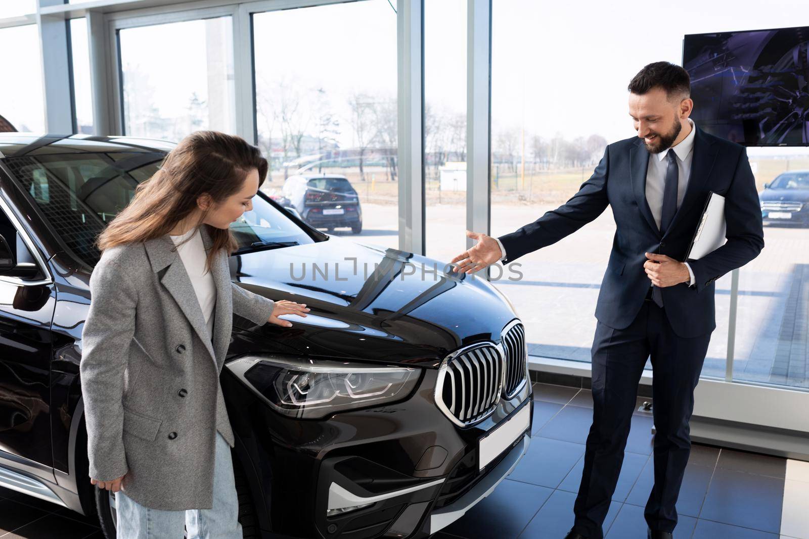 a young woman in a car dealership chooses a new car together with a manager, car rental concept by TRMK