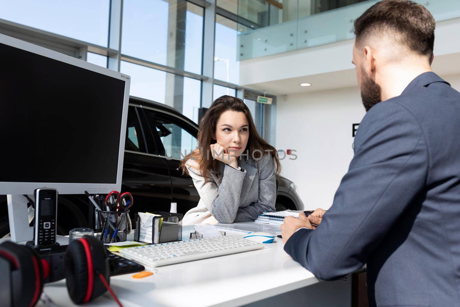 a young woman buyer in a car dealership learns from a consultant the details of a transaction for buying a car on credit.