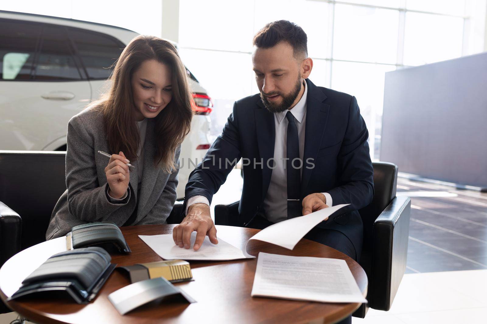 young woman buys a new car in a car dealership and signs documents.