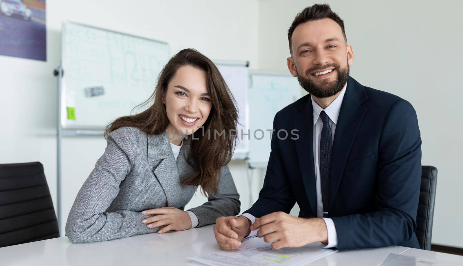 man and woman employees of the company in presentable business clothes with a smile look at the camera while sitting at the table by TRMK