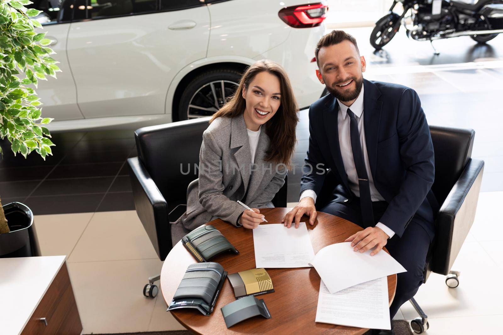 car dealership manager and satisfied buyer on the background of new cars in the dealership.
