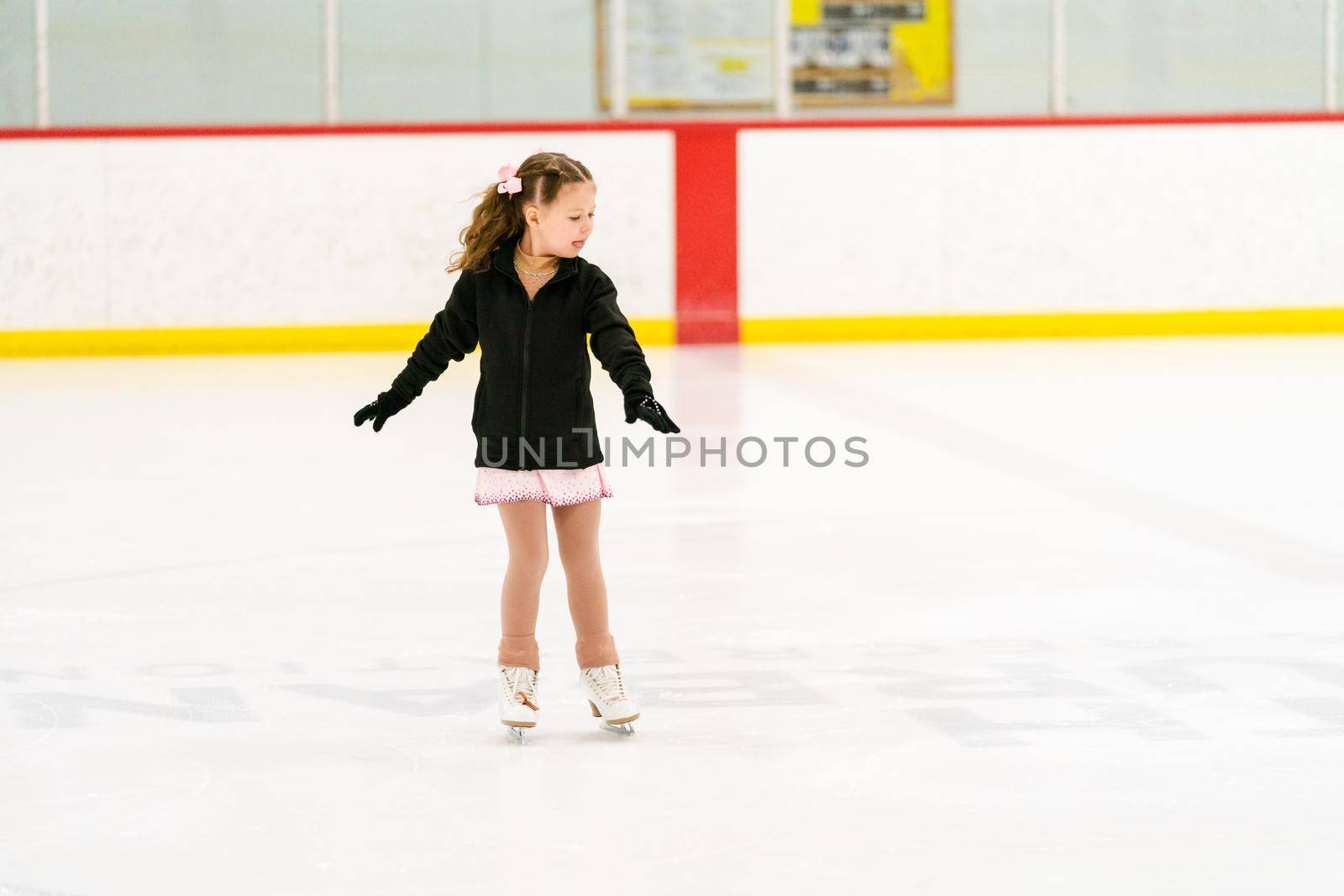 Little girl practicing figure skating on an indoor ice skating rink.