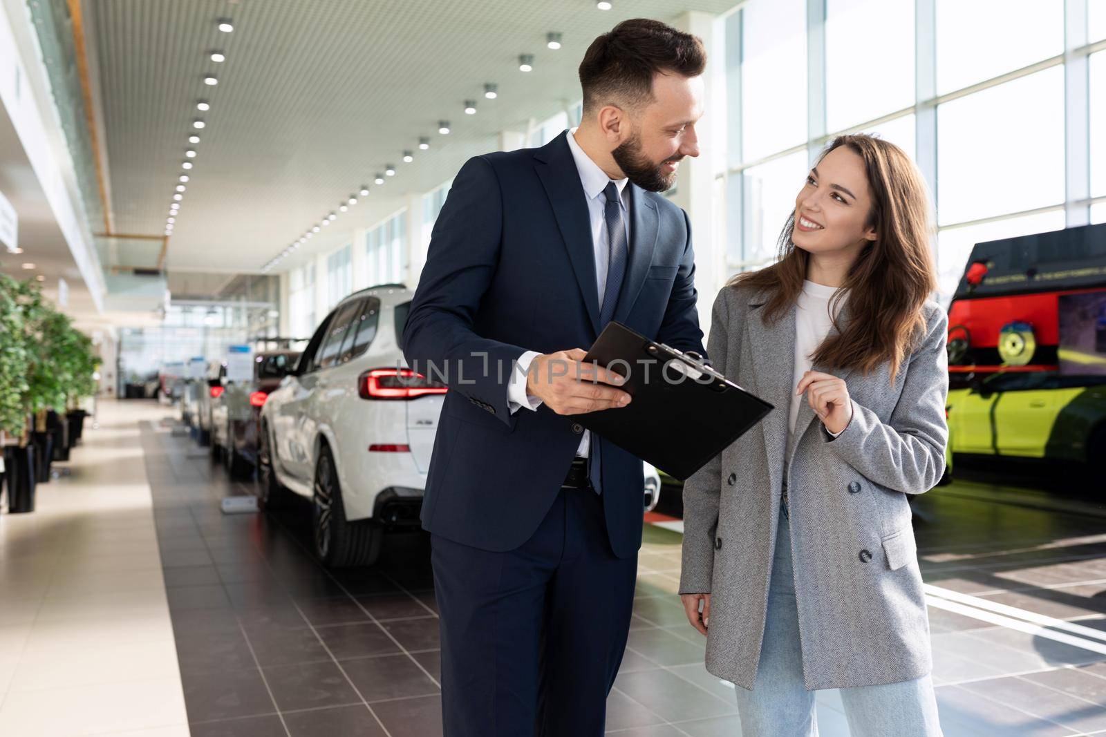 an employee of a car dealership helps to sort out a car insurance buyer woman.