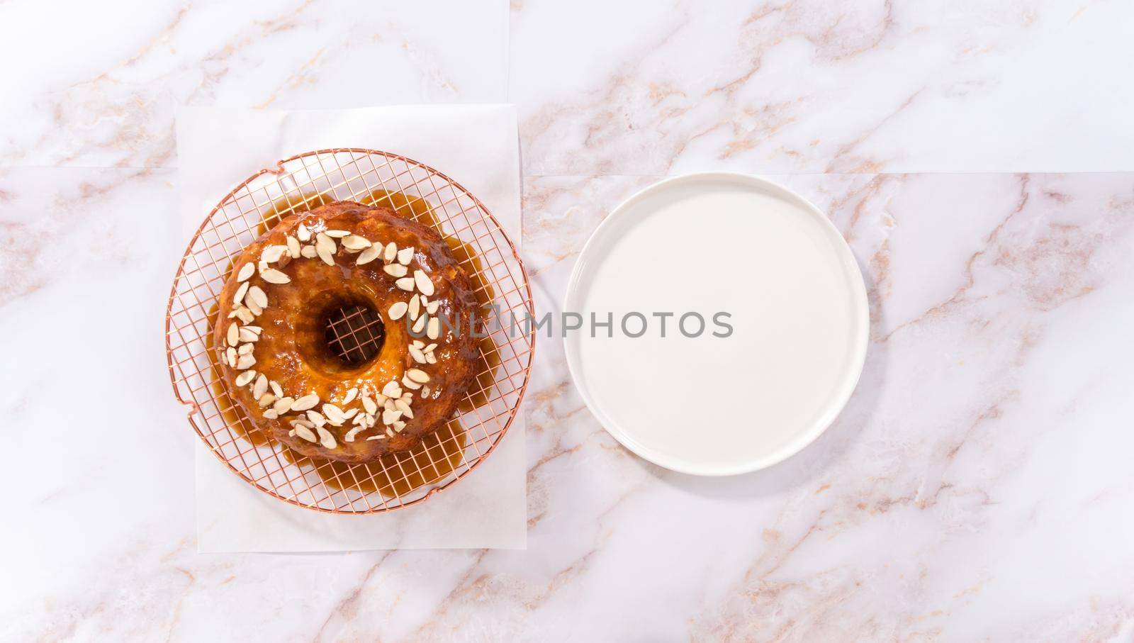 Flat lay. Glazing homemade caramel glaze over freshly baked apple bundt cake and garnishing with sliced almonds.