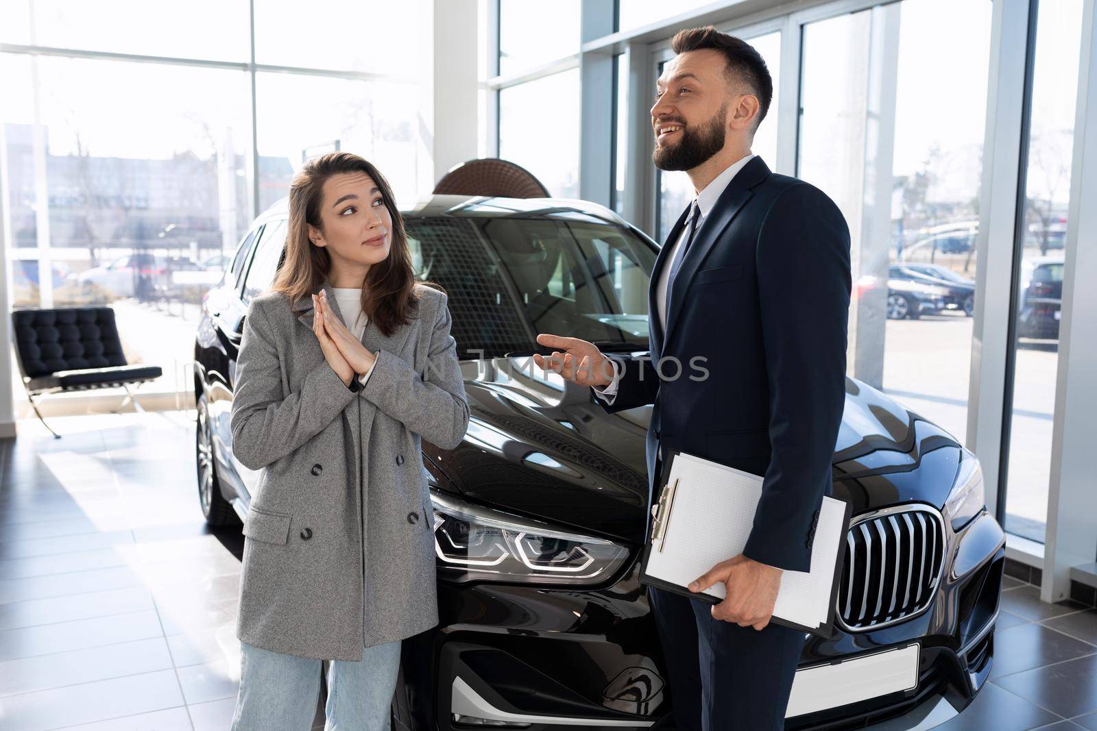 car dealership employee talking about new car model to woman buyer.