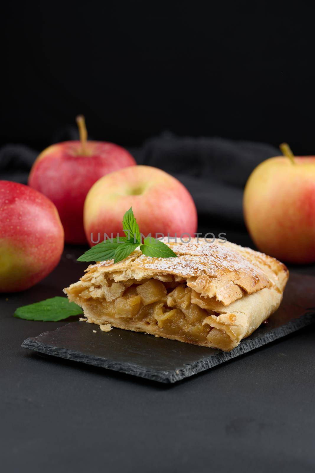 Baked strudel with apples sprinkled with powdered sugar on a black board