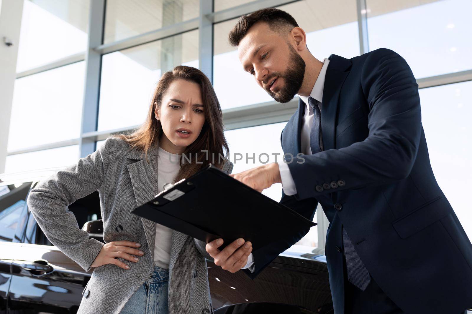 displeased young woman in car dealership arguing with car dealer by TRMK