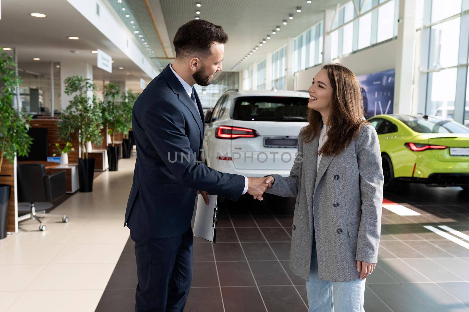 young woman buyer and seller of car dealership making a deal and shaking hands.