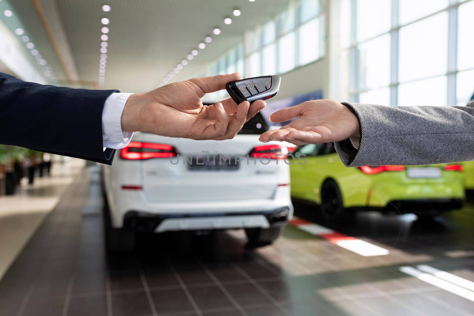 handing over the keys close-up by the seller of the car dealership to the buyer on the background of new cars.