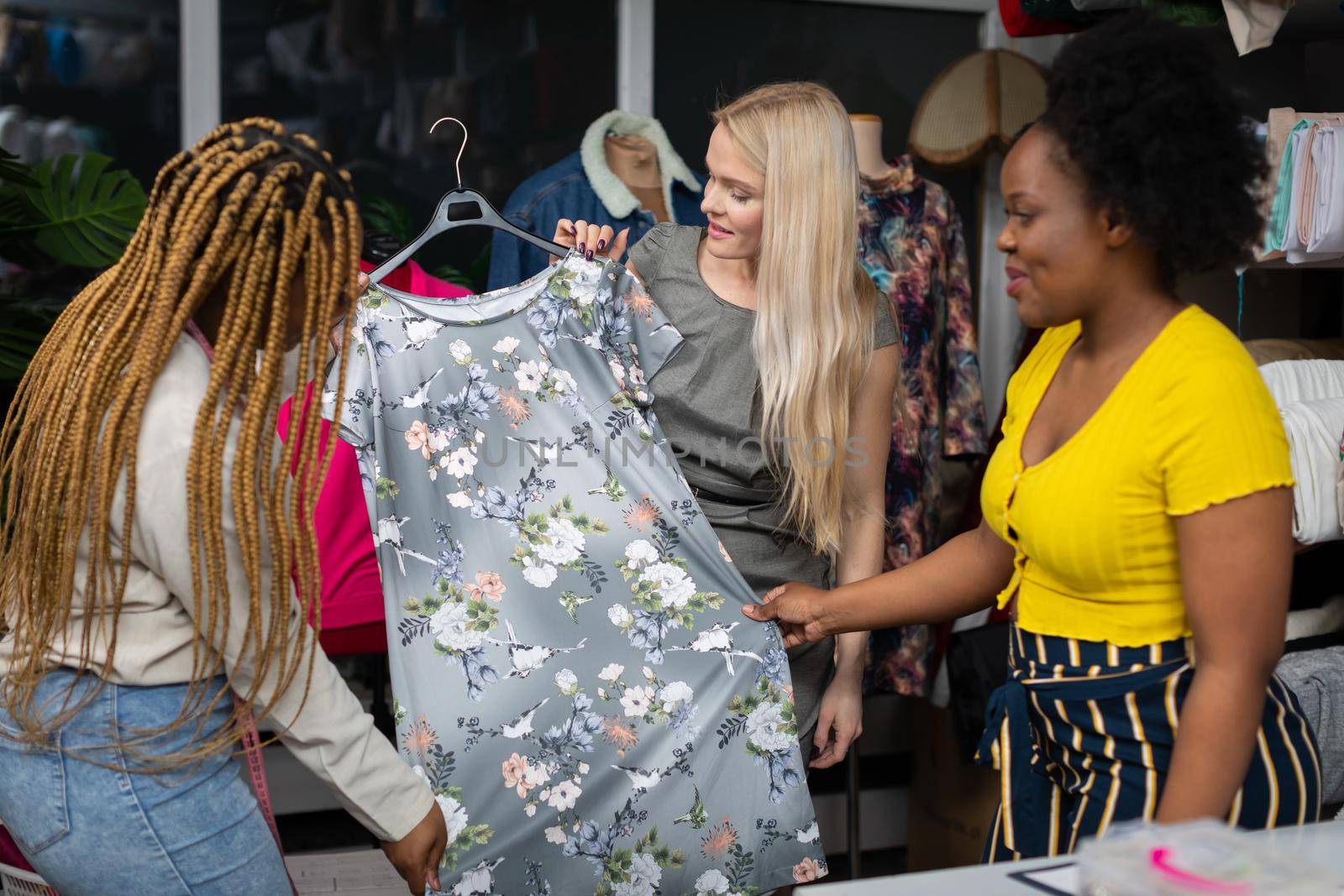 A blonde woman looks at a dress with a floral pattern. A dark-skinned shopper. by fotodrobik