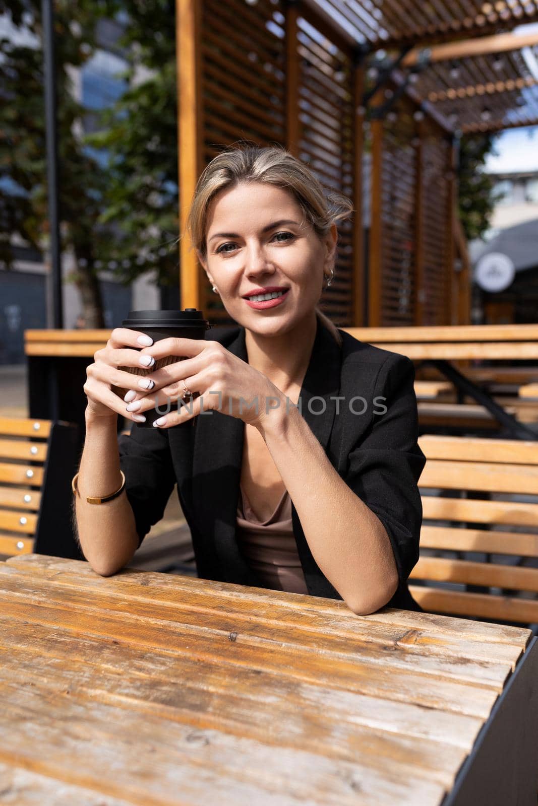 young middle-aged woman with a smile looking at the camera in a street cafe with a cup of coffee by TRMK