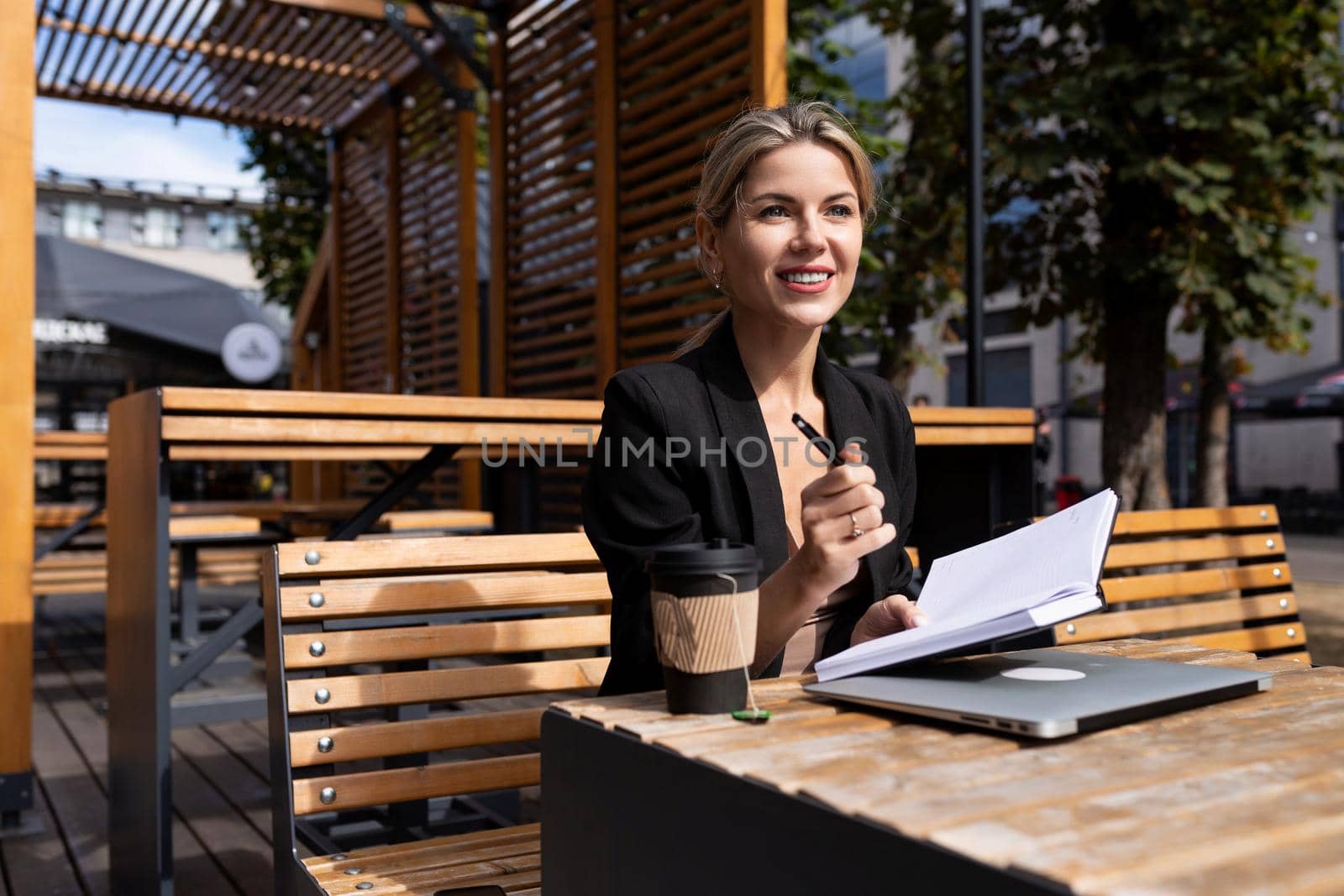 young woman specialist works outdoors with a laptop and makes notes in a diary.