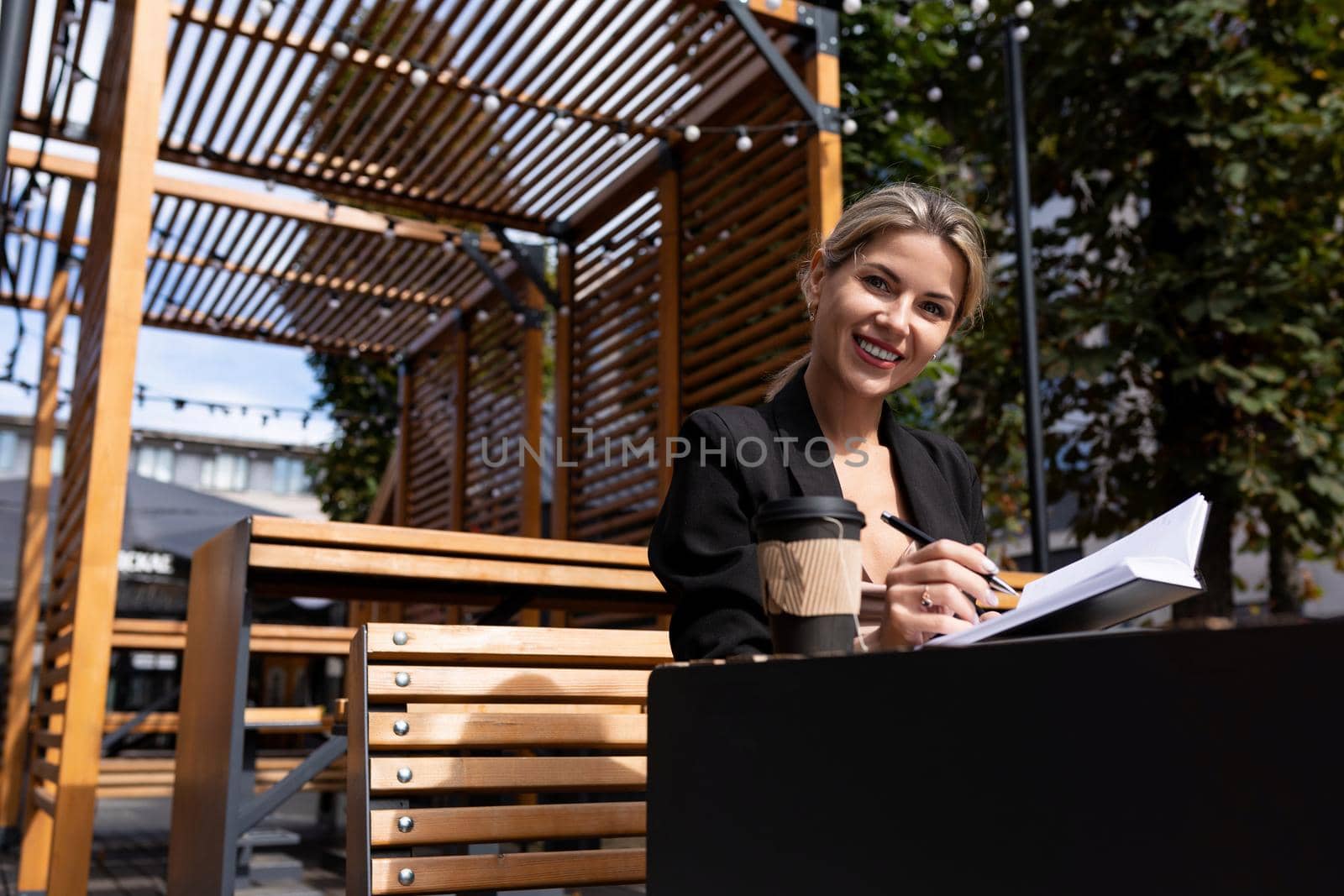 successful businesswoman working outdoors drinking coffee and making notes in her diary.