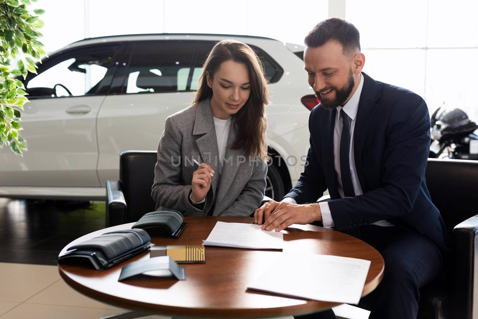 a young woman buys her first car in a car dealership and signs a contract to buy insurance.