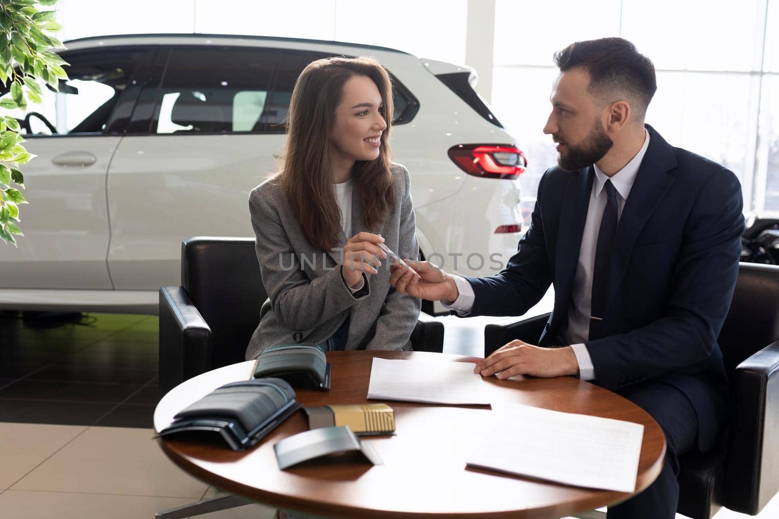 male manager selling a new car to a young woman in a car dealership, car rental concept by TRMK