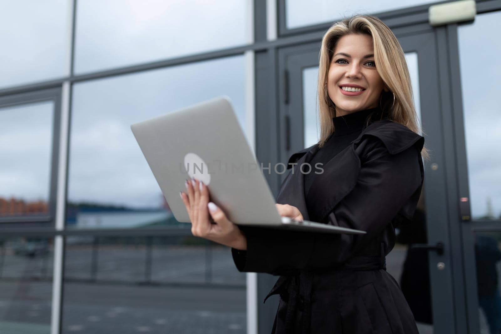 successfully confident businesswoman works online on a laptop against the backdrop of an office building.