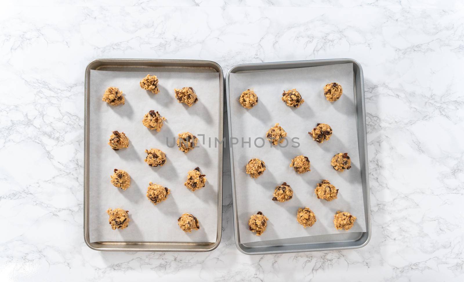 Flat lay. Scooping cookie dough with dough scoop into a baking sheet lined with parchment paper to bake soft oatmeal raisin walnut cookies.