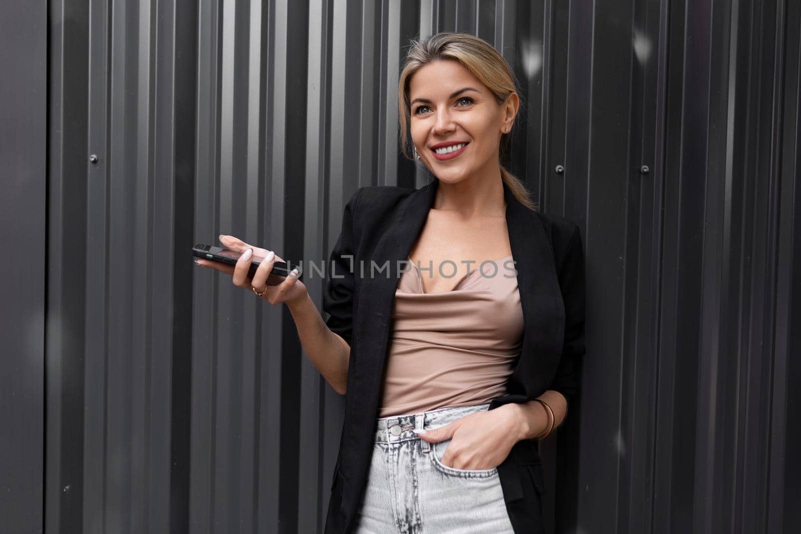 charming middle-aged business woman with a charming smile against a gray wall in her hands holds a mobile phone.