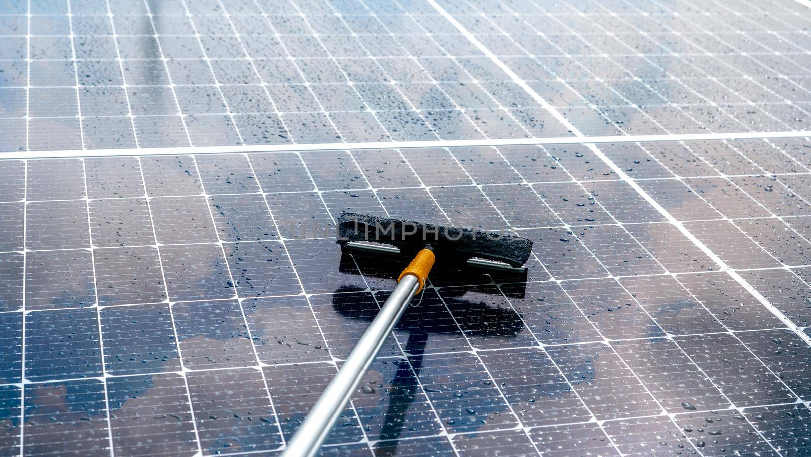 Cleaning solar panel with microfiber mop on wet roof. Solar panel or photovoltaic module maintenance service. Sustainable resource. Solar power. Green energy. Sustainable development technology. by Fahroni