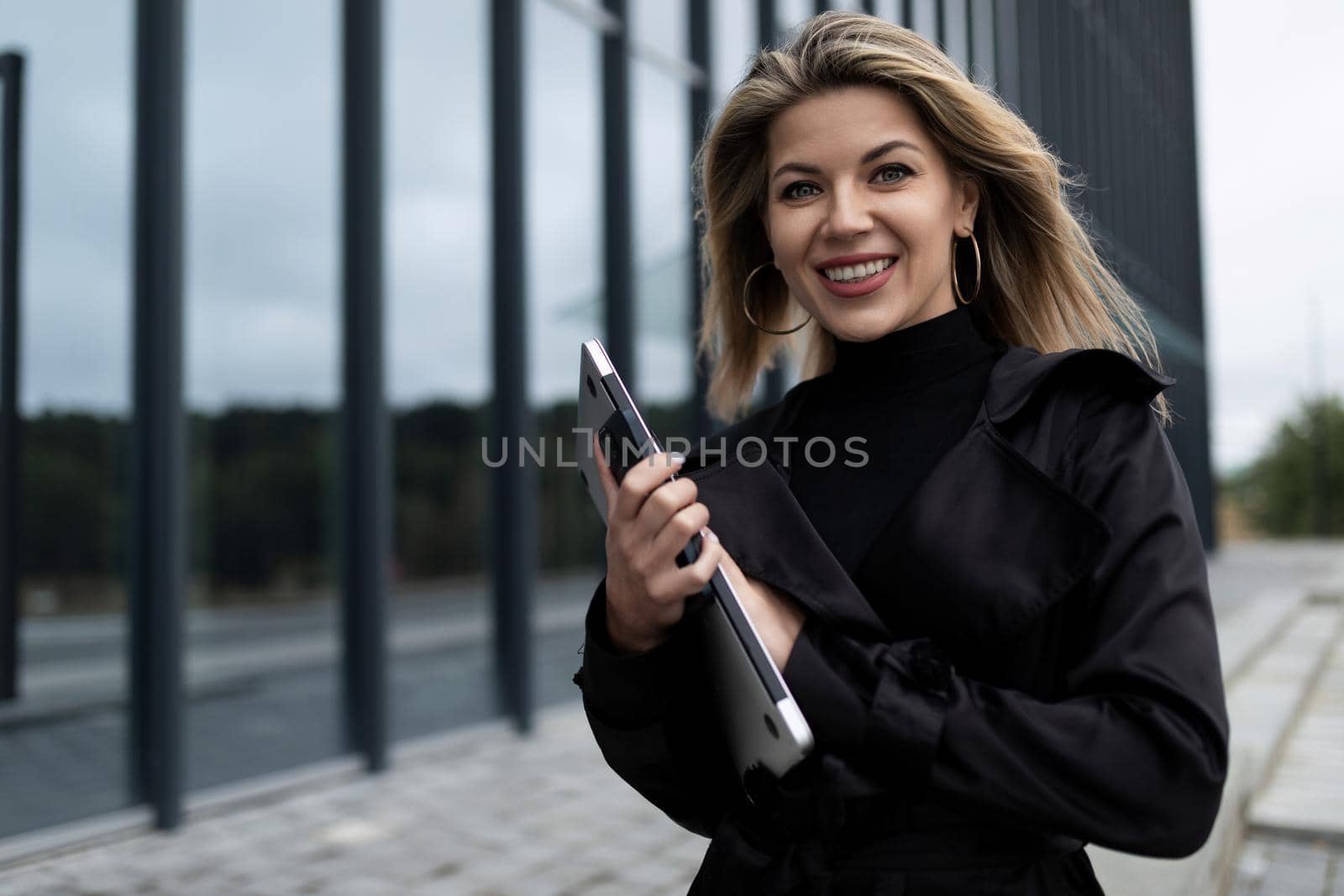office employee woman with a tablet in her hands hurries to work with a smile on her face against the backdrop of the city.