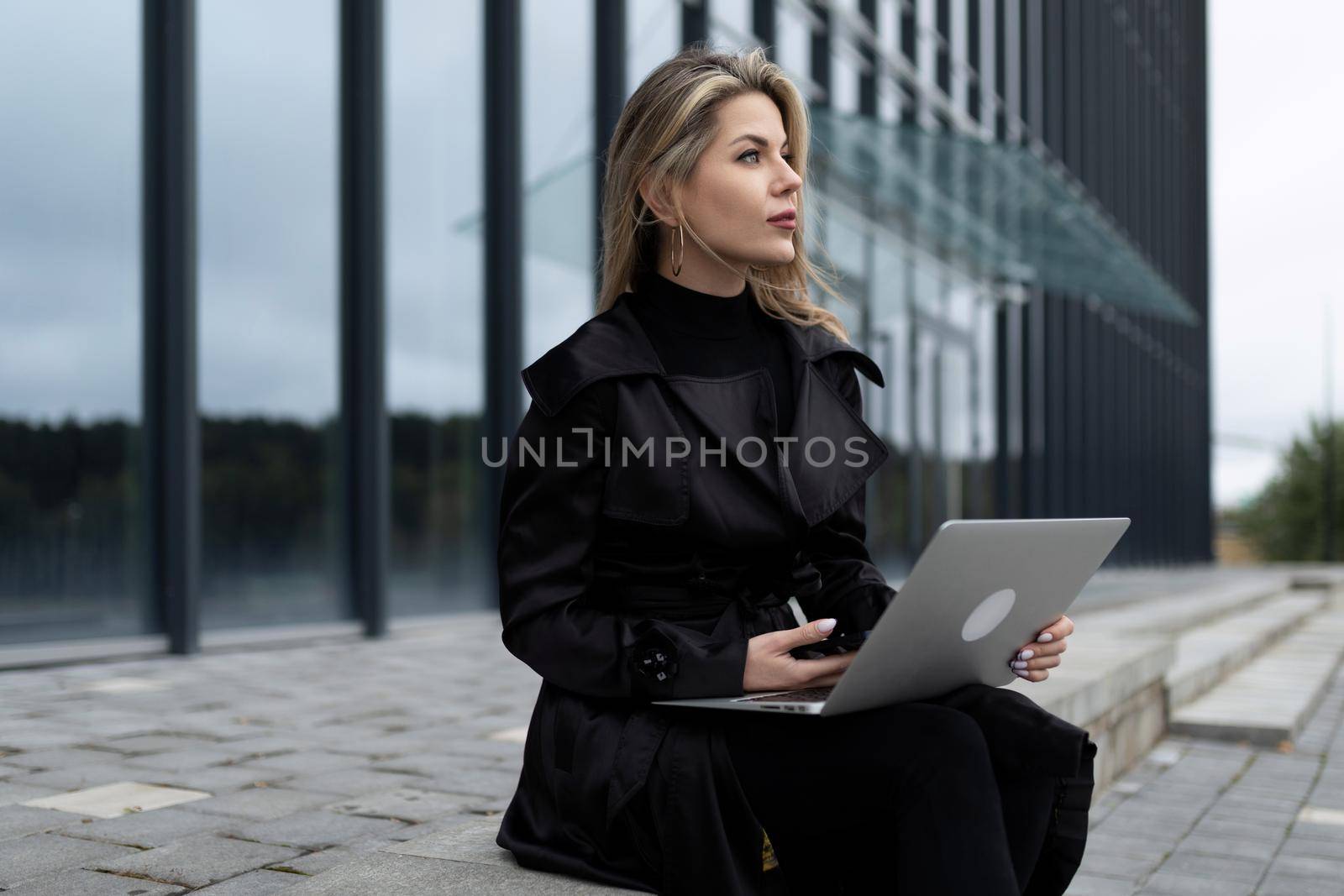 modern successful business woman works online on the background of an office building.