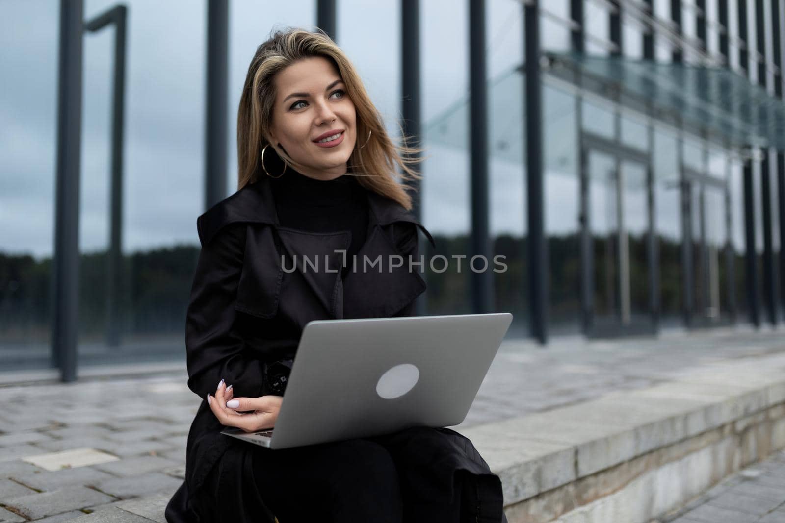 successful business woman works online on a laptop against the backdrop of an office building.