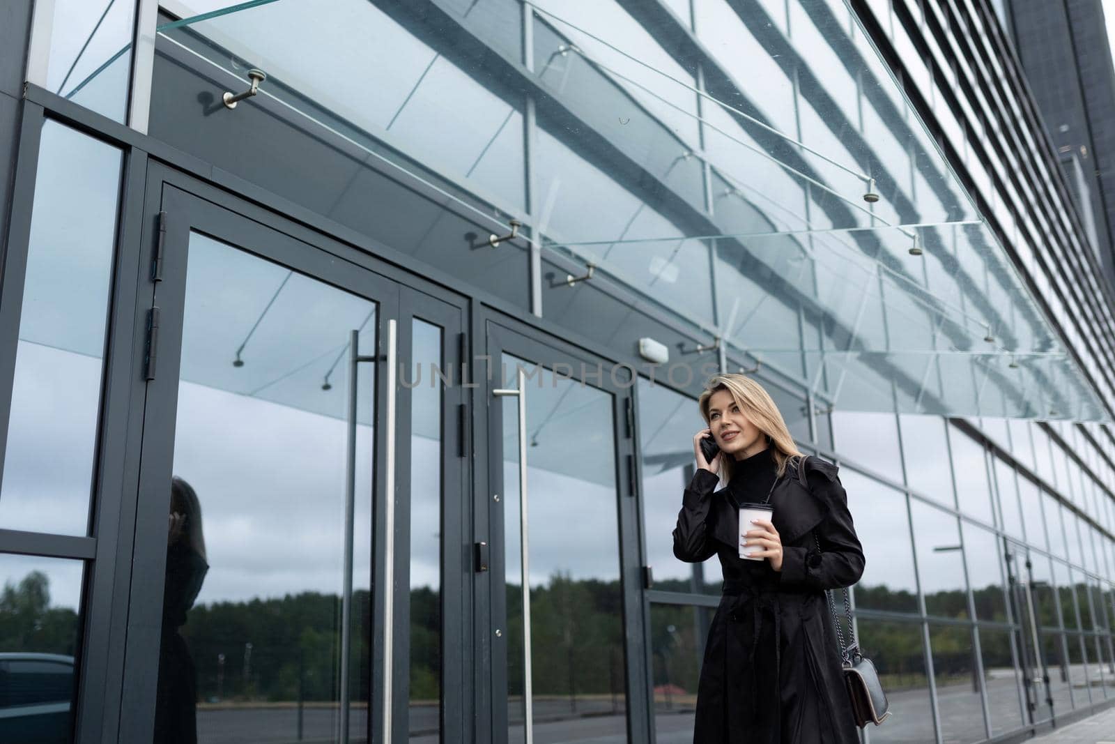 successful business woman goes to work in the office with a glass of coffee by mobile phone.