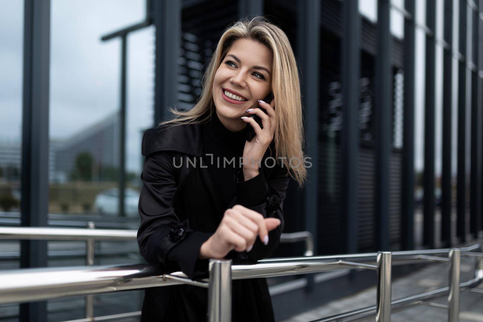 a woman manager speaks on a mobile phone against the backdrop of an office modern building made of glass.