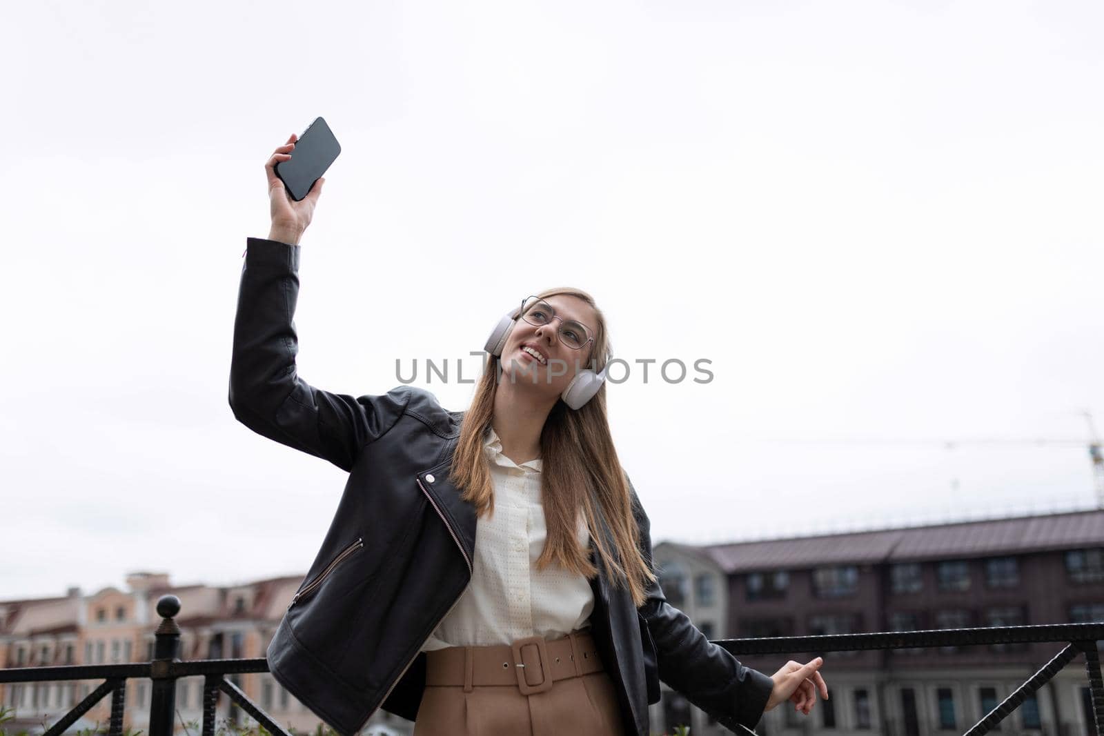 happy young woman with a mobile phone in her hands and headphones dances against the backdrop of the city panorama.